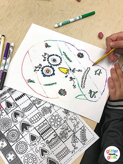 student coloring his sugar skull using day of the dead symbols from worksheet