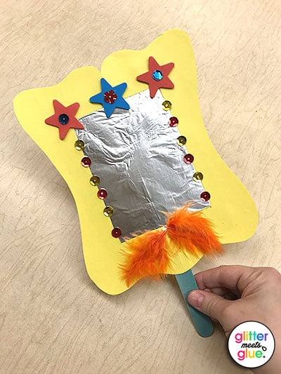 Decorated hand mirror art project with sequins, foam shapes, and feathers.